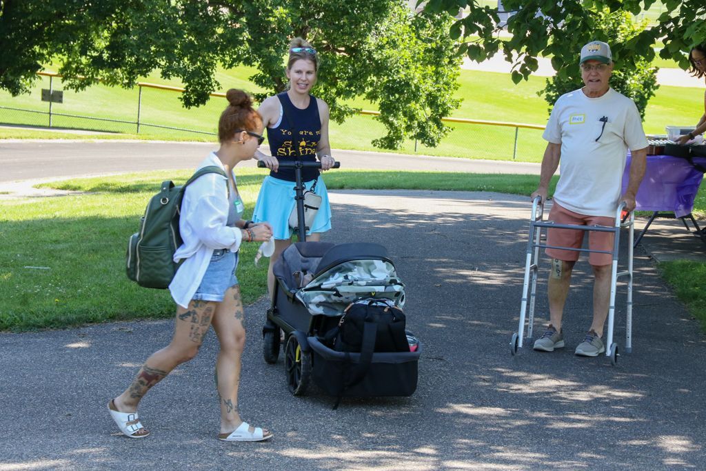 Woman walking, pushing a stroller with a woman on a scooter, and a man using a walker. Outdoors.