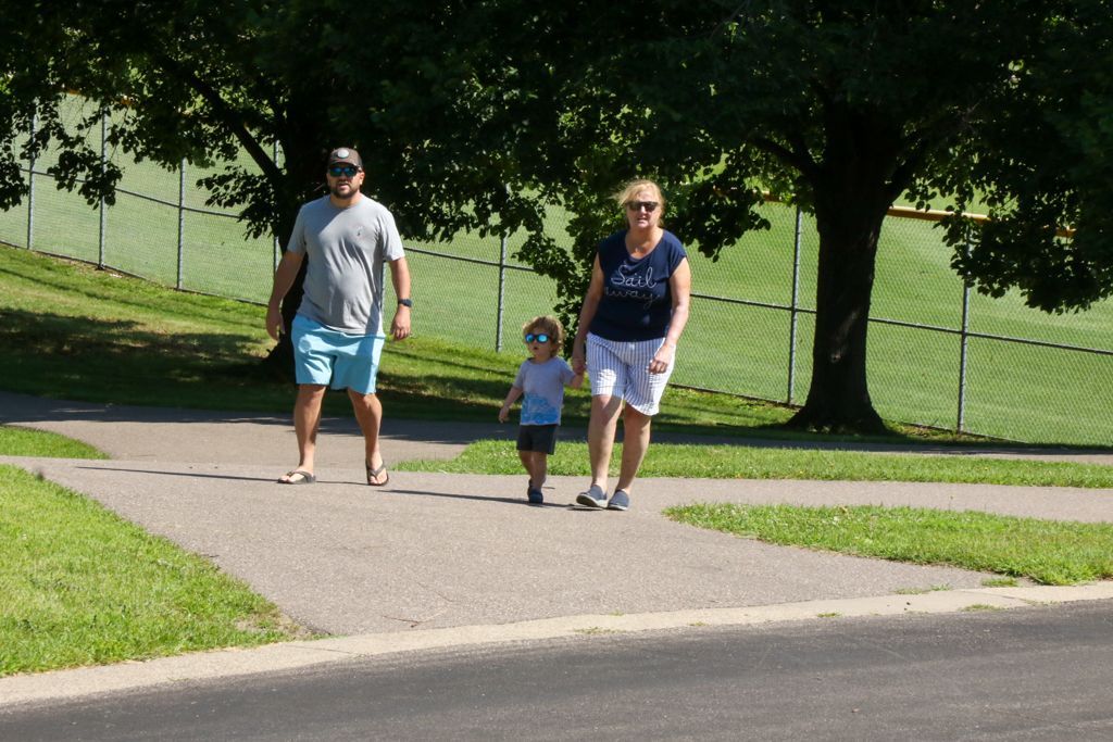 Family walking on a paved path in a park; sunny day.