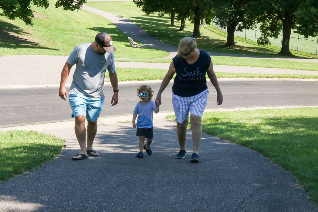 Family walking on a paved path in a park; sunny day.