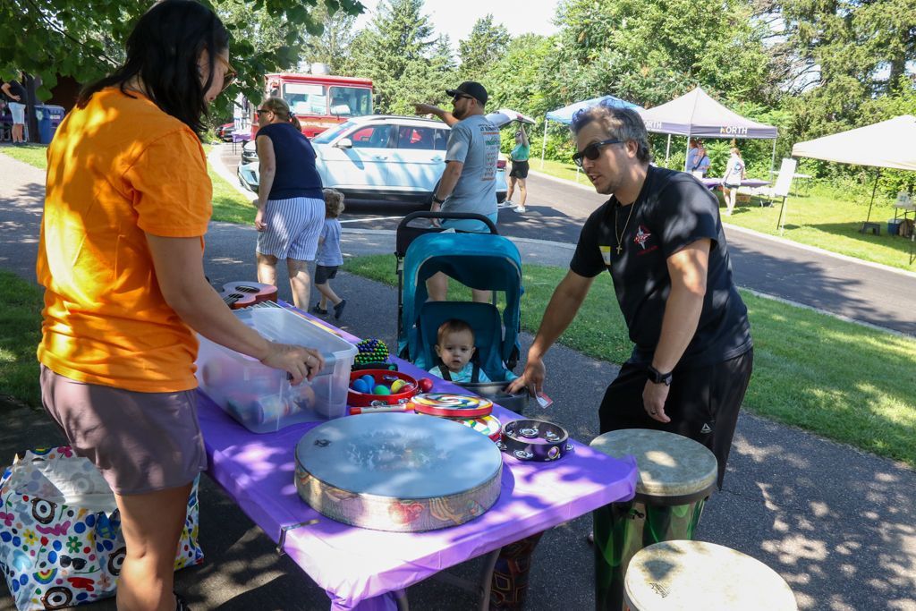 People at a table with musical instruments, a child in a stroller, and a food truck in a park.