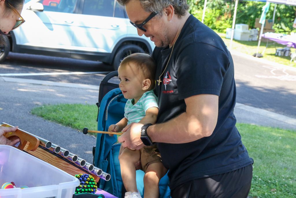Man holding baby sitting in a stroller, both looking at a fishing game. Outdoors.