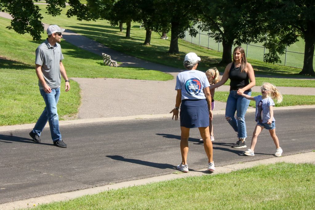 People walking on a paved path in a park. One man, two women, and two children are present.
