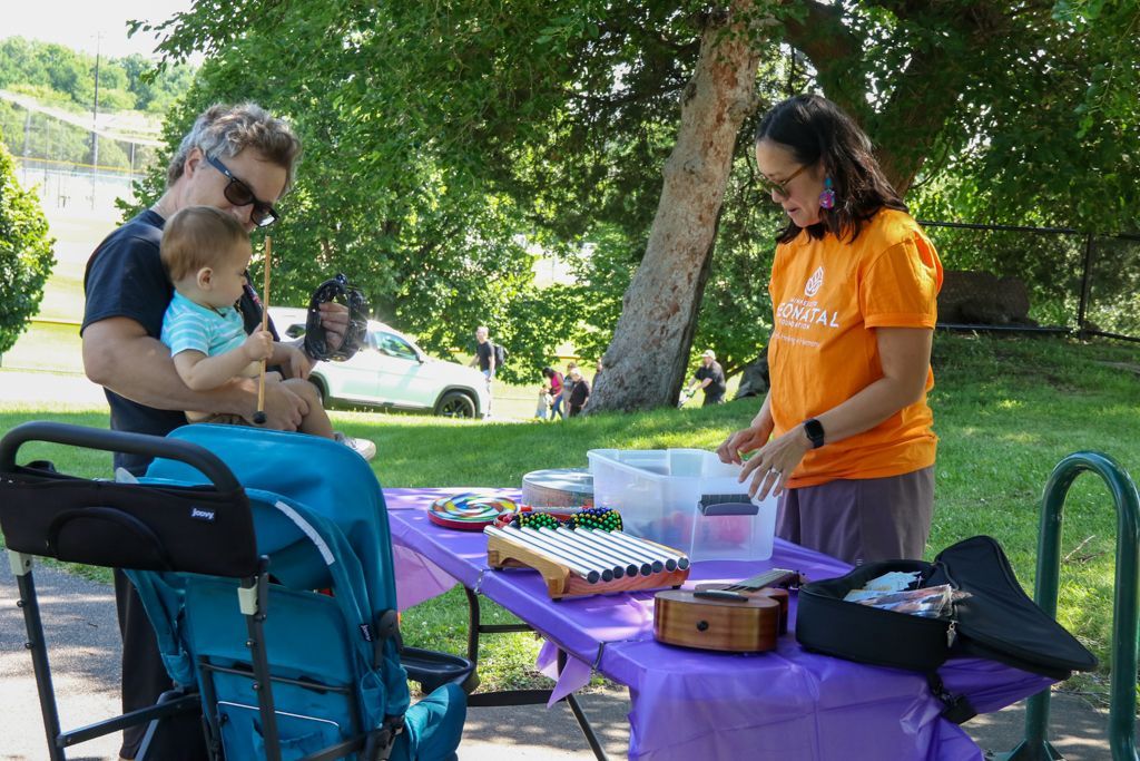 Man holding child near stroller, woman at table with musical instruments, outdoors.