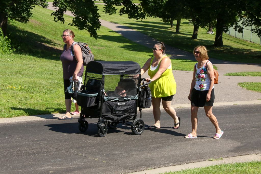 Three people walking on a paved path in a park; one pushing a double stroller.