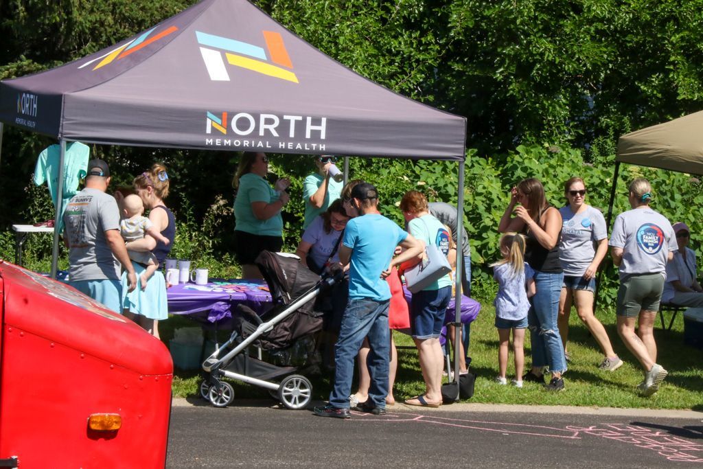 People at a booth with a purple tent. A stroller and red vehicle are in the foreground.