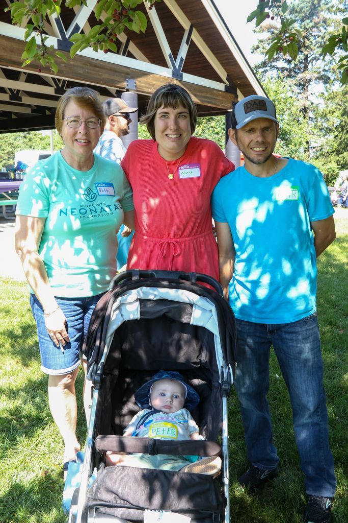 Three adults and a baby in a stroller pose outdoors; the woman in the middle is wearing a red dress.