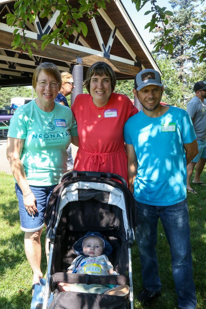 Three adults and a baby in a stroller posing for a photo outdoors.