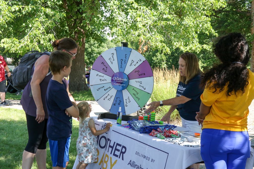 People playing a game at an outdoor event. A large prize wheel sits on a table.