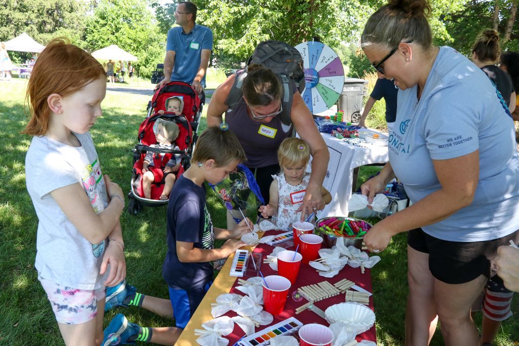 Children and adults at an outdoor craft table, engaged in a hands-on activity with cups and supplies.