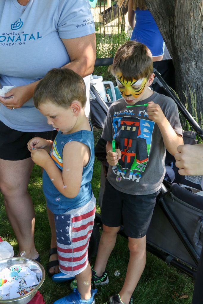 Two children outside, one with tiger face paint, one in American flag shorts, near adults.