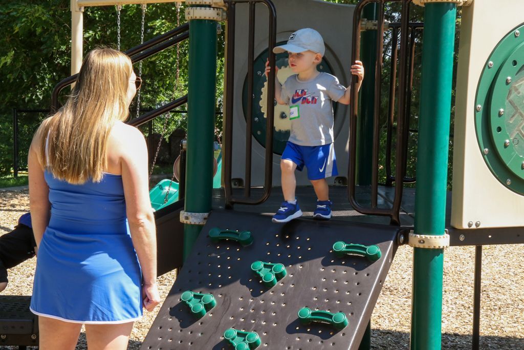 Woman watching a child climb a playground rock wall.