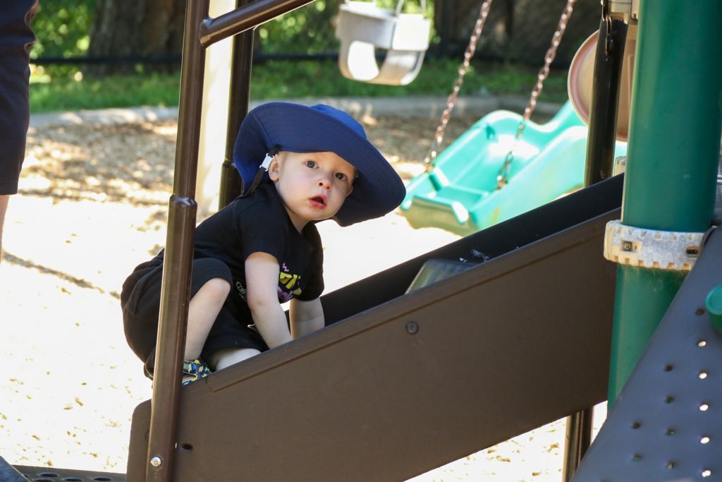 Child in blue hat climbing a playground ramp, looking up.