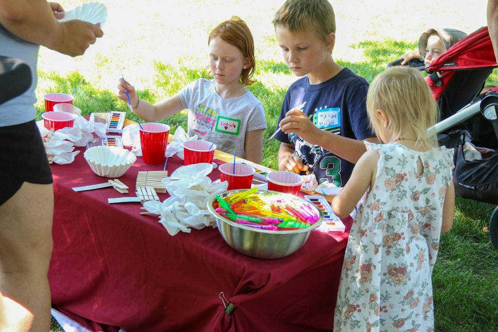 Children at a picnic table with food and drinks; red cups, sunny day.