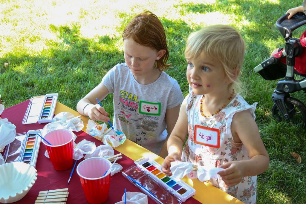 Two children painting outdoors at a table with art supplies.