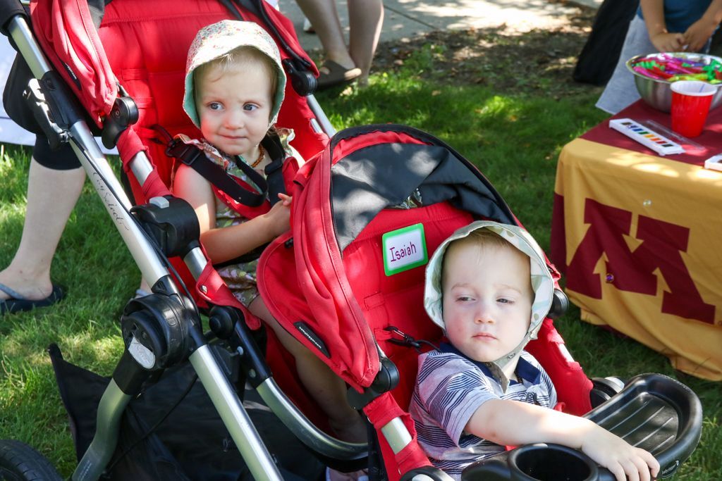 Two toddlers in a red stroller outdoors, both wearing sun hats.