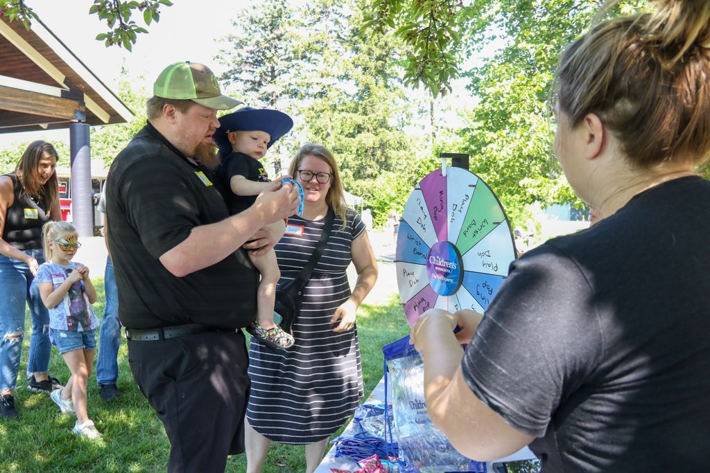 People playing a game at an outdoor event. A man holds a baby near a prize wheel as another person spins it.