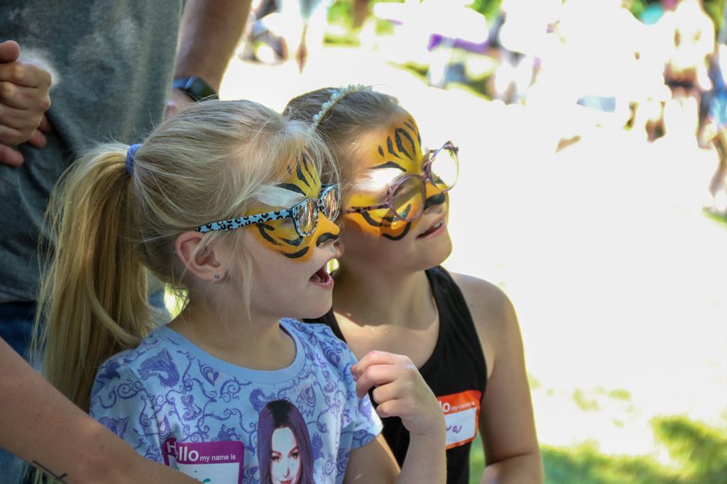 Two children with tiger face paint looking upward at an outdoor event.