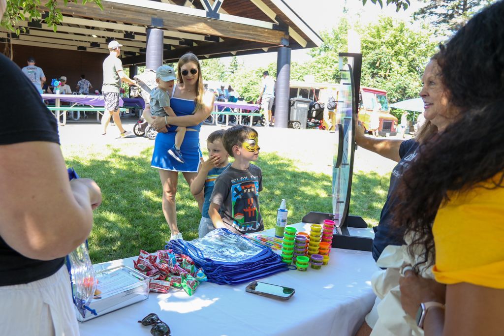 People at a table with face paint and supplies, including a woman holding a baby and a child with face paint on.