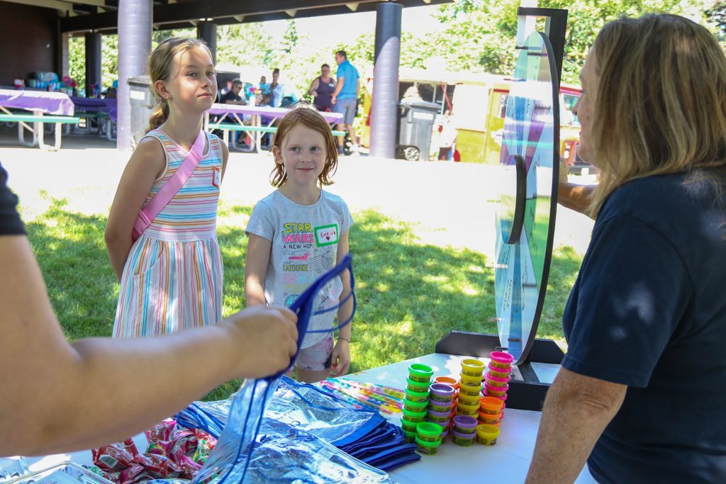 Two girls and an adult woman at a carnival game, outdoors.