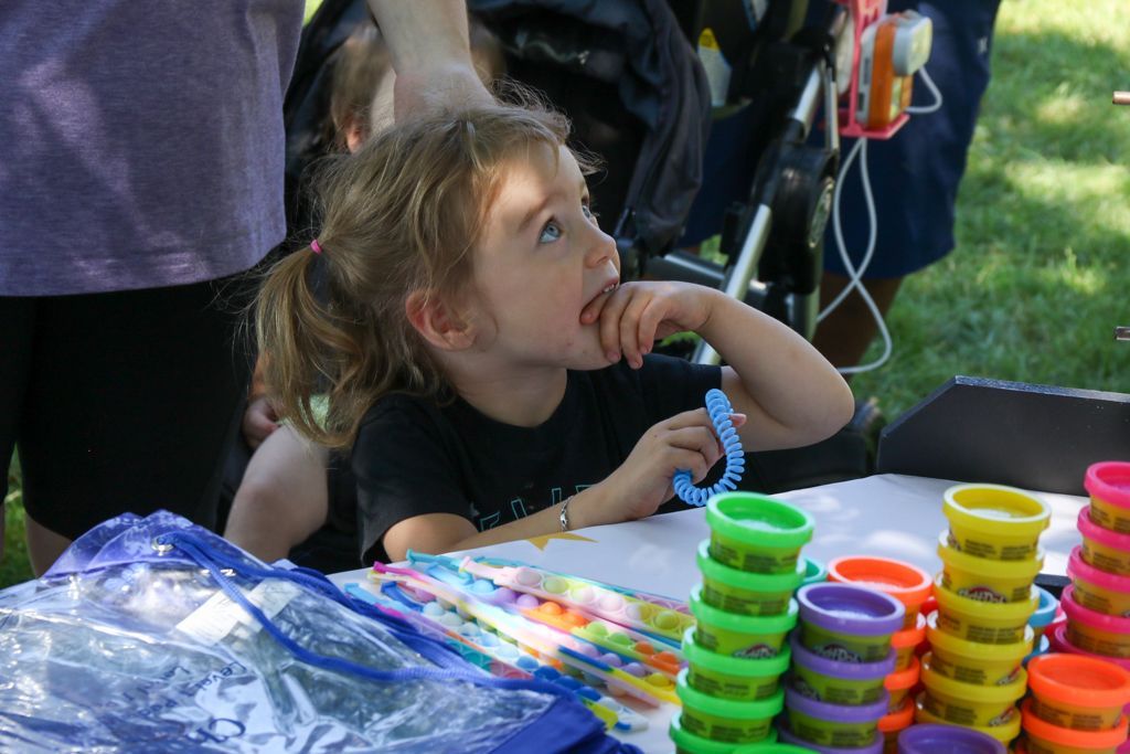 Girl at a table with playdough, looking upwards with a hand near her mouth.