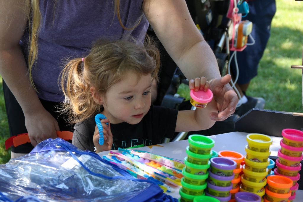 Child playing with colorful Play-Doh at a table, supervised by an adult.