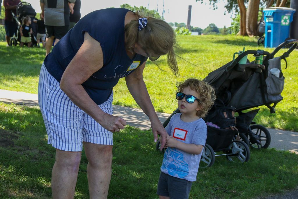 Woman in blue shirt and striped shorts with a young child in sunglasses outdoors, stroller nearby.