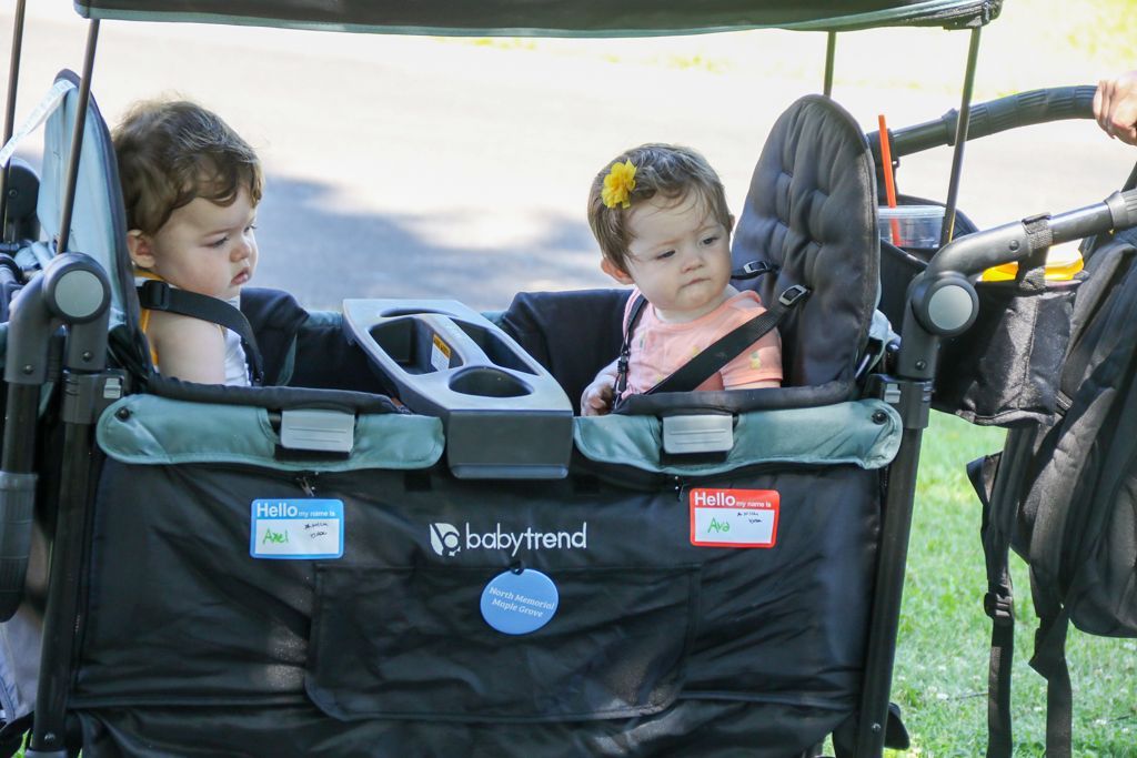Two babies sit in a Baby Trend wagon with drinks holder, one with a flower in hair.