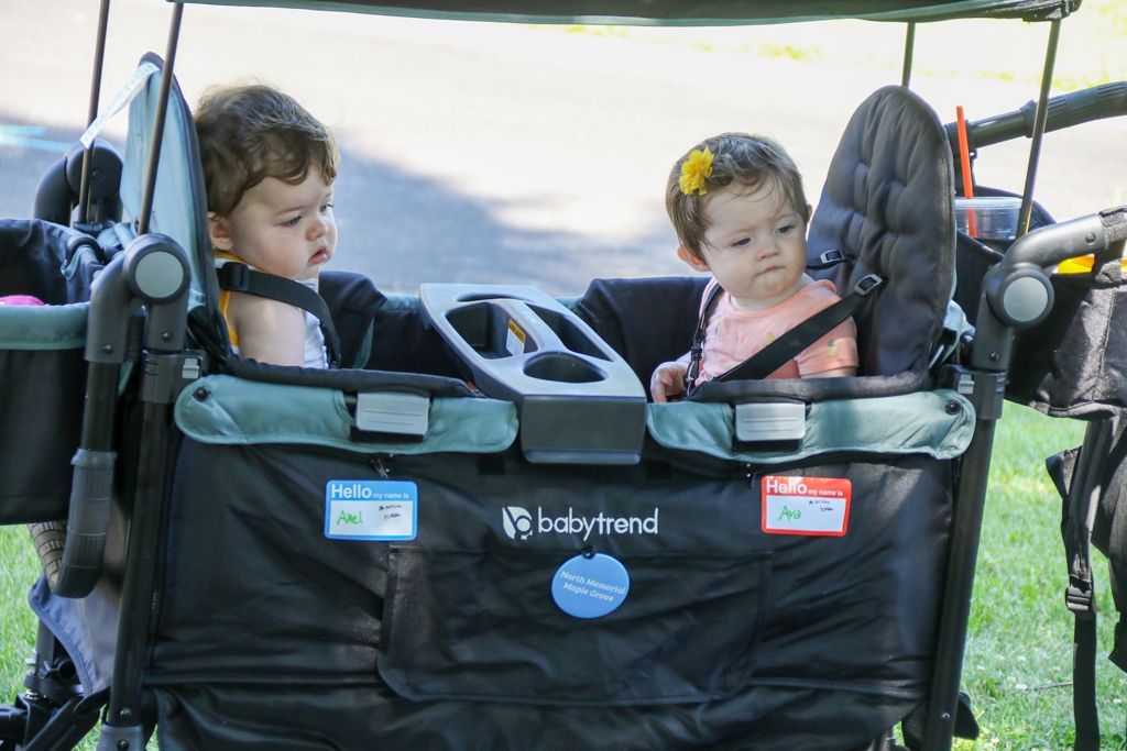 Two toddlers in a black and green stroller wagon with a canopy.