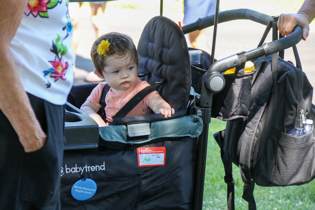 Baby sitting in a stroller, wearing a peach shirt, with a flower in their hair.