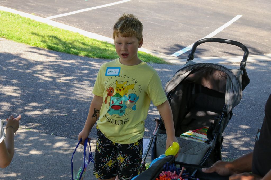 Boy in yellow shirt with Pokemon graphic standing next to stroller, holding toys outside.