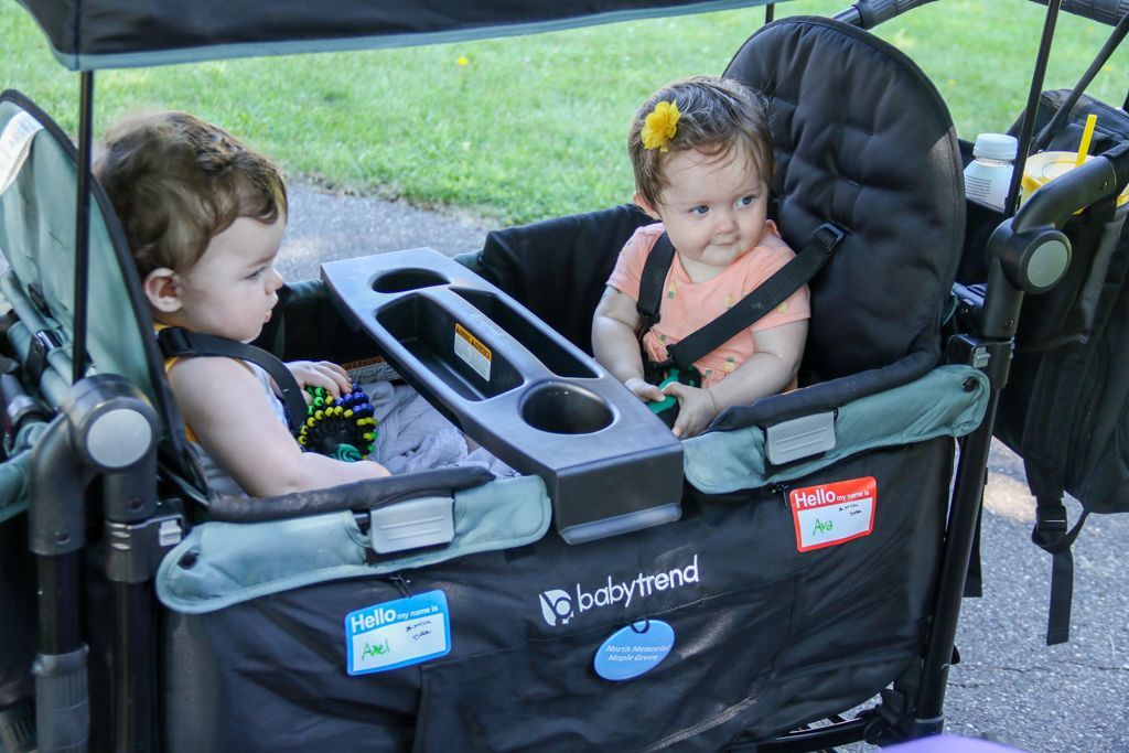 Two babies in a green stroller with canopy. One baby looks left, the other right.