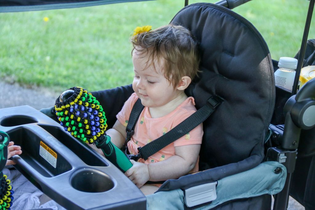Baby in a black and green stroller, holding a toy, sitting outside.