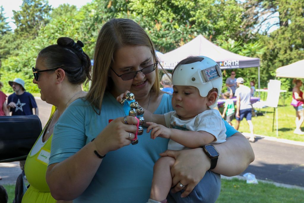 Woman holding a baby wearing a helmet, both looking at a small trophy outdoors.