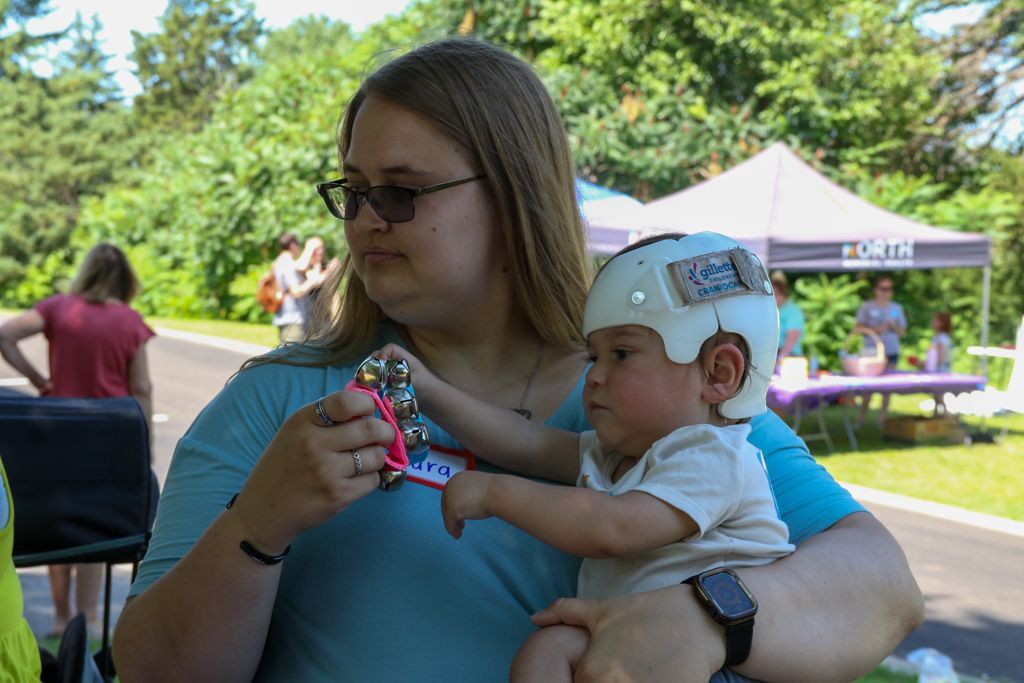 Woman holding baby with a white helmet, outdoors, sunny day.