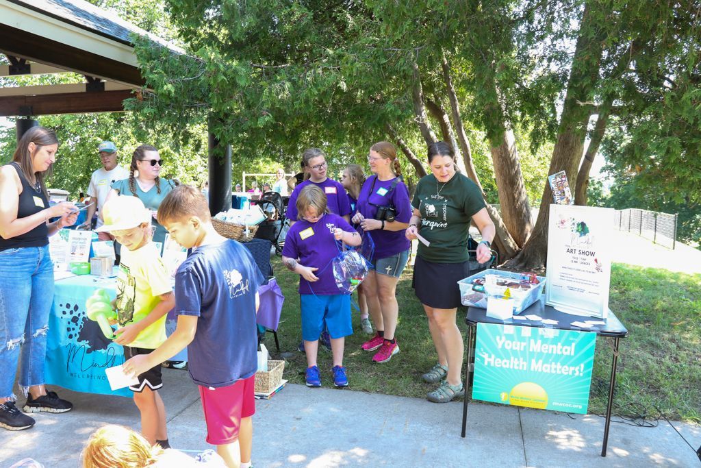 People at an outdoor event with tables and signs related to mental health.