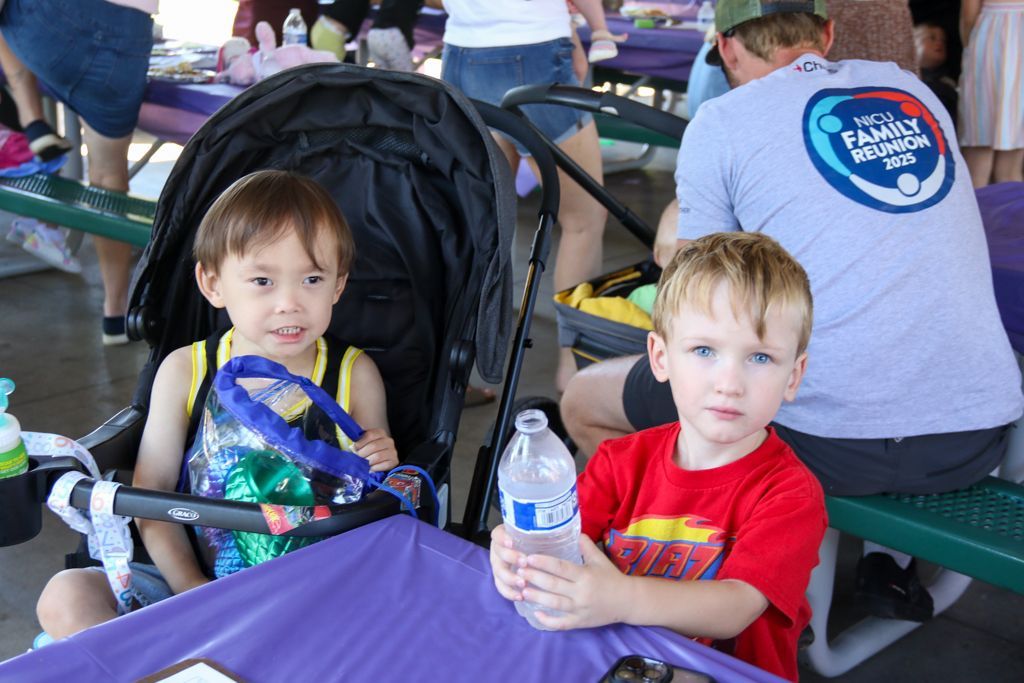 Two young children at a picnic table, one in stroller, one holding water bottle.