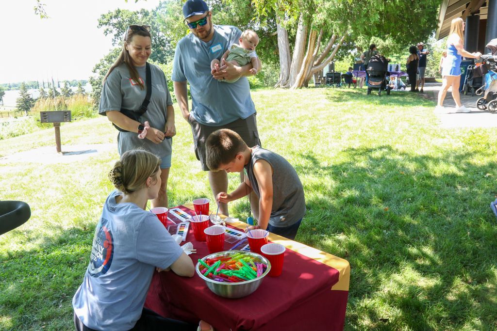 People at an outdoor table with treats, a family watches a boy reach for something.