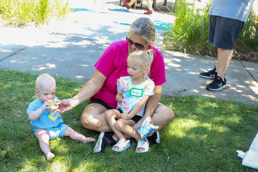 Woman sitting with two young children on grass, sunny day.