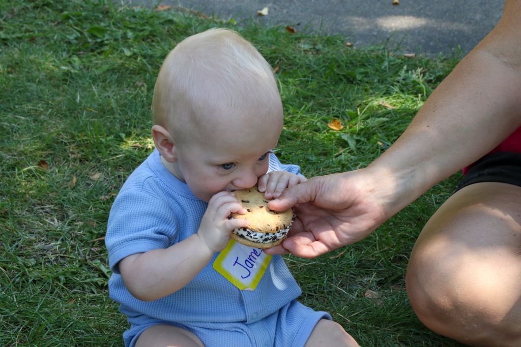 Baby eating cookie outdoors, held by adult.