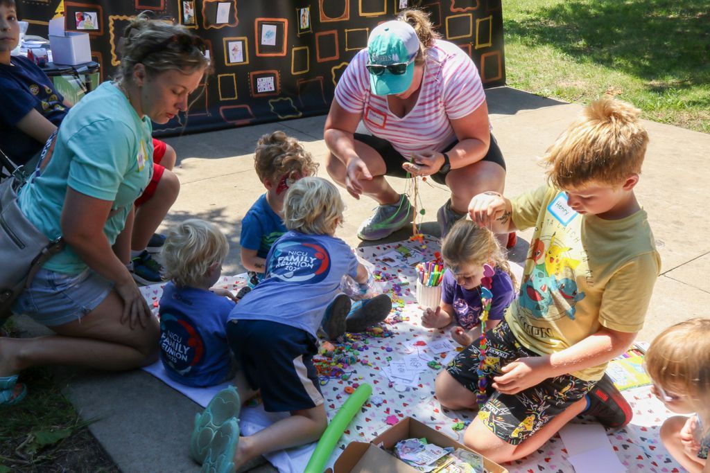 People and children on the ground, making crafts at a table outdoors.
