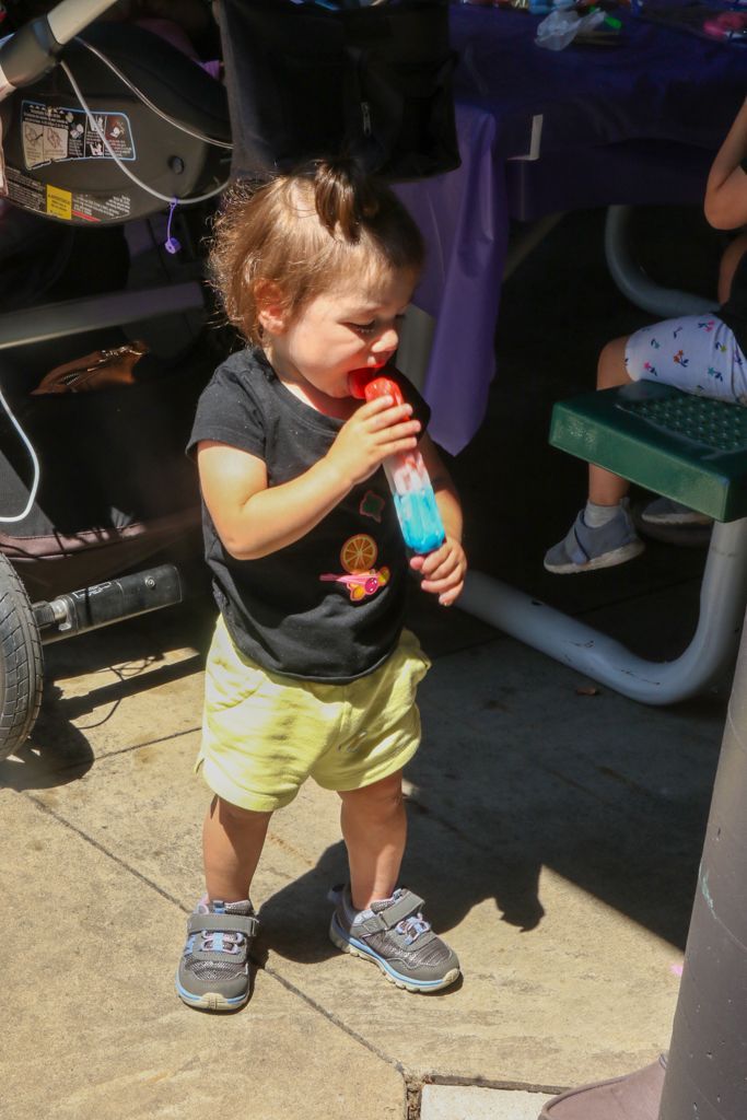 A young child in yellow shorts eating a blue popsicle outside.