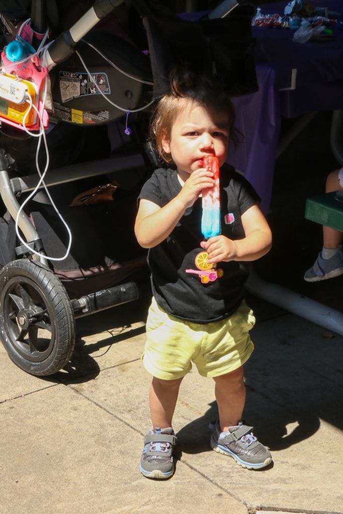 Child holding a popsicle, standing outside near a stroller.