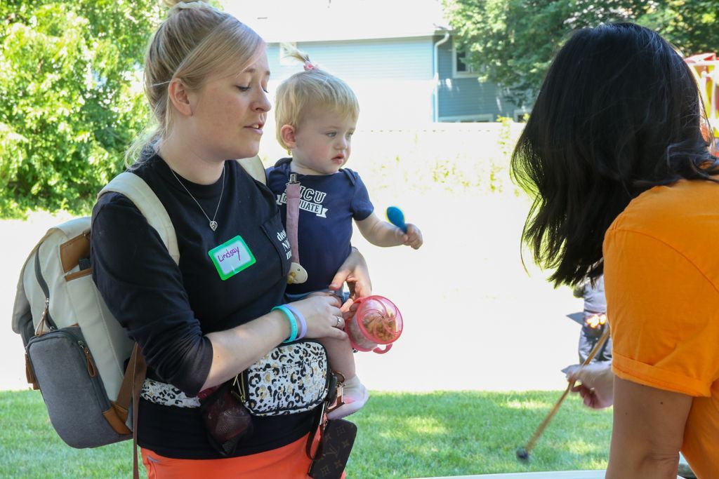 Woman holding child, talking to another person outdoors.