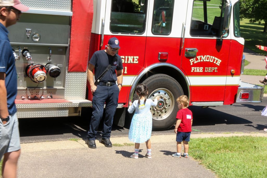 Firefighter with two children near a red fire truck. Children are looking up at the firefighter.