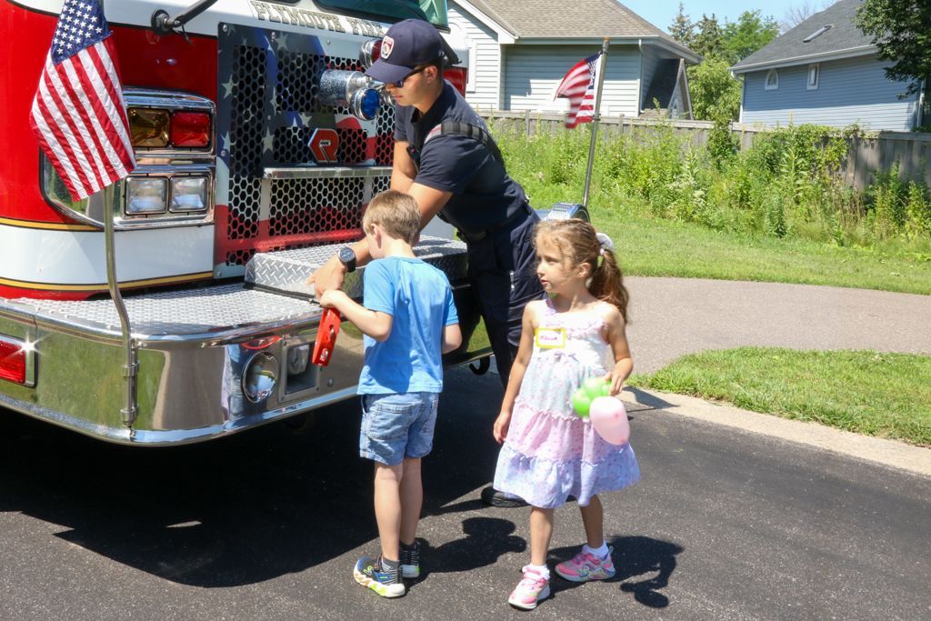 Firefighter showing two children the back of a fire truck with an American flag.