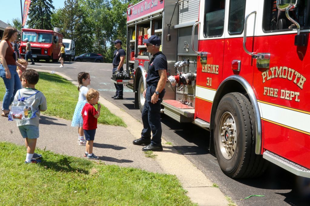 Firefighters show children a red Plymouth Fire Dept. truck; a food truck is in the background.