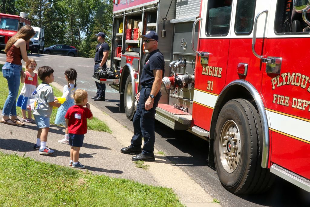 Children with adults near a red fire truck at an event; Plymouth Fire Dept. on side.