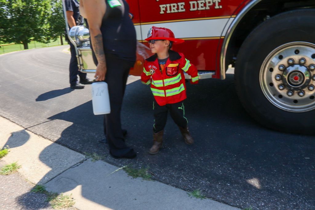 Child in firefighter uniform near fire truck, smiling.