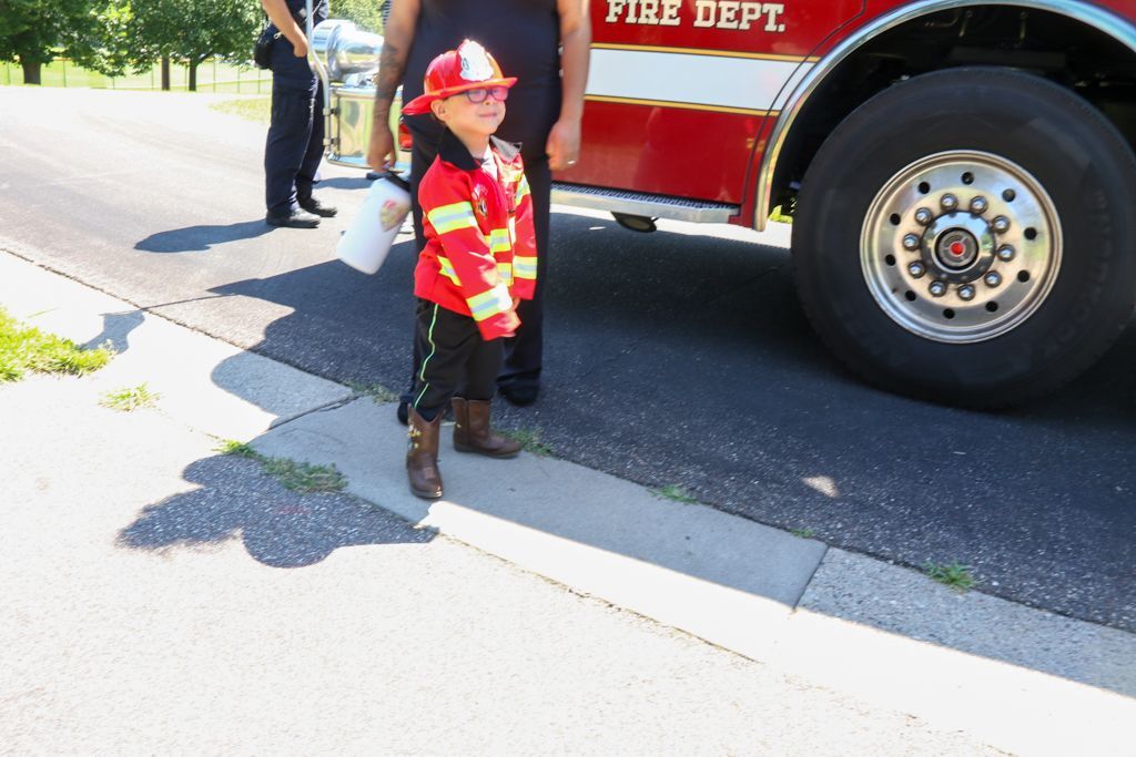Child in firefighter costume stands next to a fire truck.