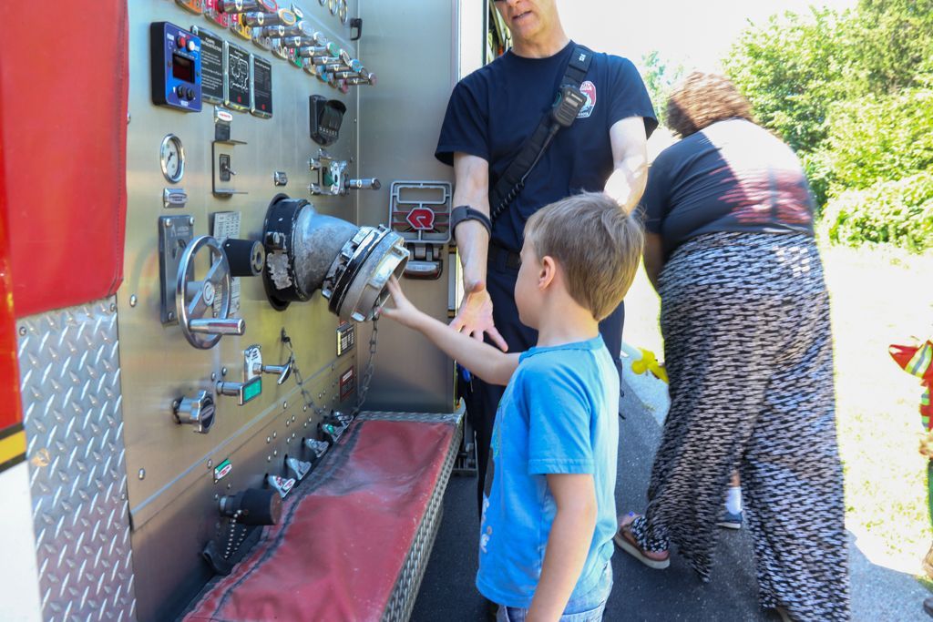 A firefighter assists a child in interacting with the controls on a fire truck.